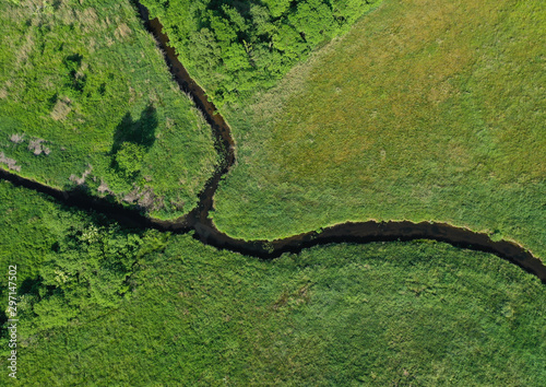Aerial drone top down view on european green meadows and forest divided by snake like river.