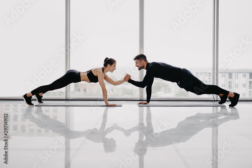 Fototapeta Naklejka Na Ścianę i Meble -  Two people that love fitness are standing on one hand in plank position and holding each other with another hand