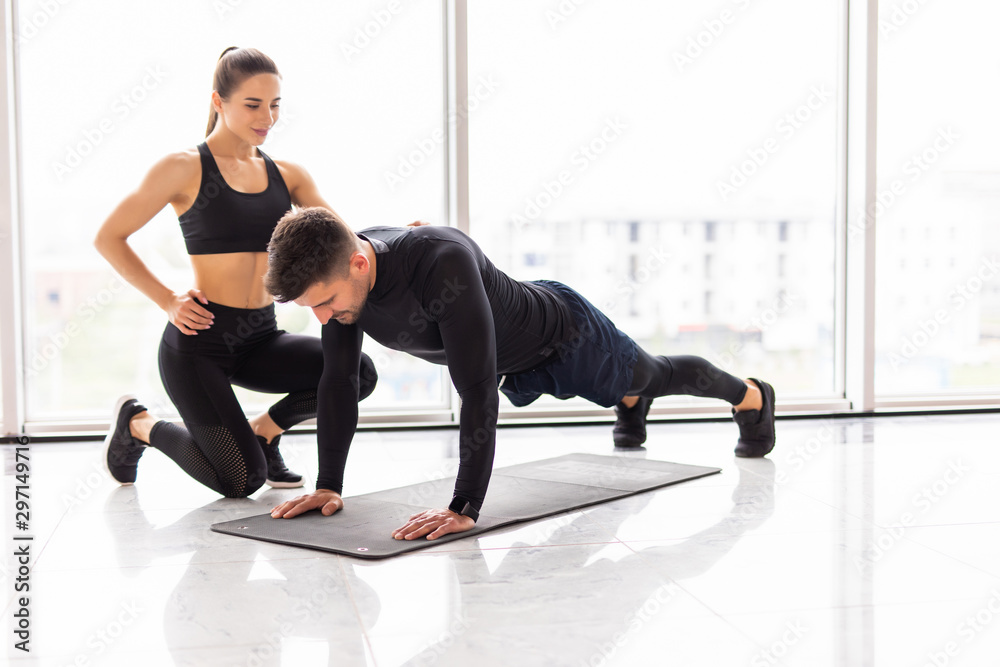 Obraz premium Sporty young couple doing plank exercise in gym. Young woman trainer work with fitness man at gym