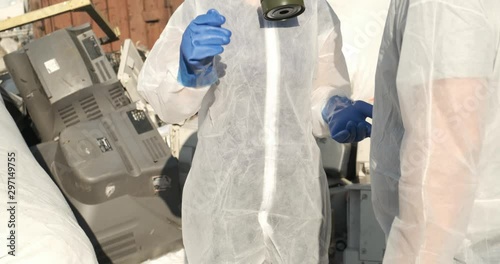 Two scientific researchers talk to each other in garbage dump, dressed in protective suits, in blue gloves and gas masks with air filter, breathing hazard, garbage in bags, global pollution of planet photo