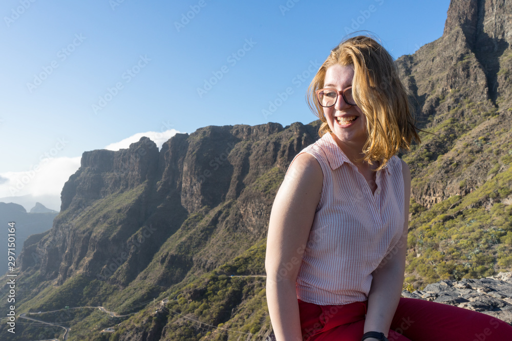 Naklejka premium Serene Cute Tourist woman, laughing and admiring the freedom and the landscape in the mountain, sitting in a rock. Model sit and smiling in the nature with excitement