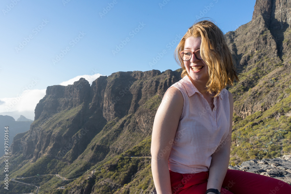 Serene Cute Tourist woman, laughing and admiring the freedom and the landscape in the mountain, sitting in a rock. Model sit and smiling in the nature with excitement