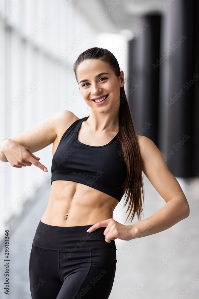 Portrait of beautiful sporty woman pointing at her abs at gym