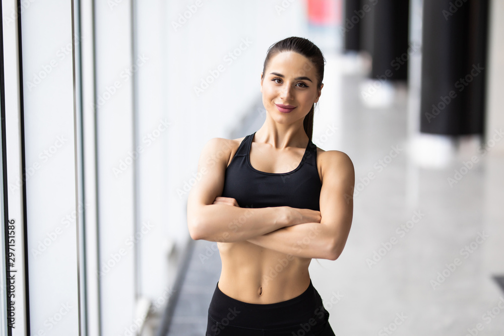 Smiling sports woman standing with arms folded and looking at camera at gym