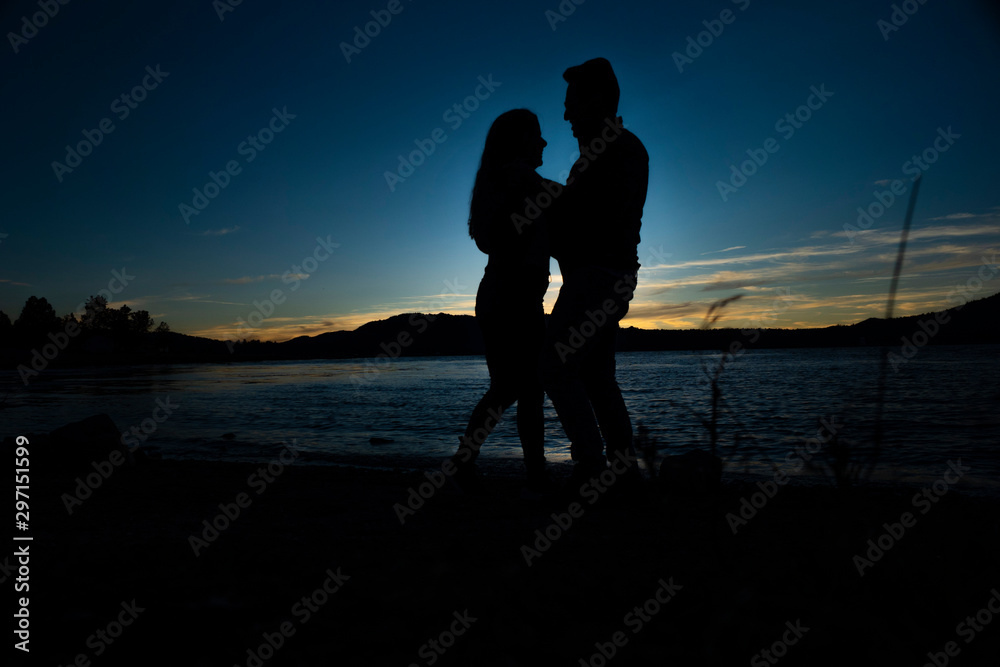 silhouette of couple dancing during sunset next to lake