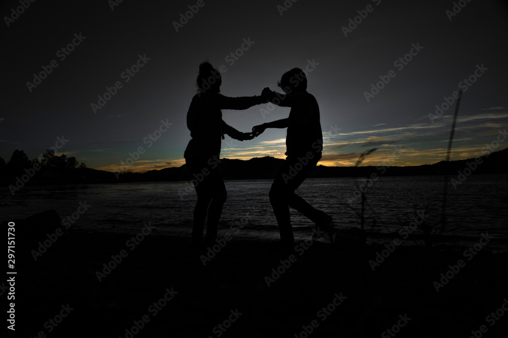 silhouette of couple dancing during sunset next to lake