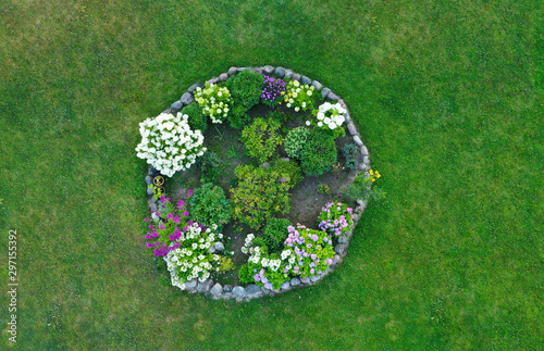 Canvas Print Aerial drone top down view on stylish round flowerbed surrounded by rock wall with violet, white and yellow blooming flowers