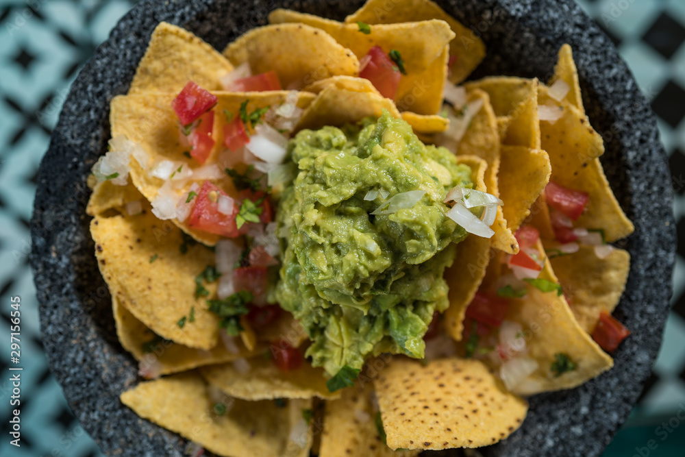 Yellow corn nacho chips garnished with ground beef, guacamole, melted
