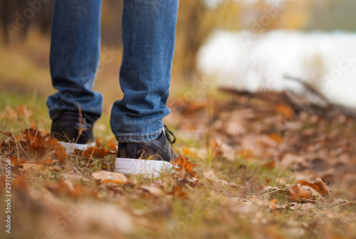 Men's feet in stylish black sneakers in autumn Park or forest. Seasonal shoes