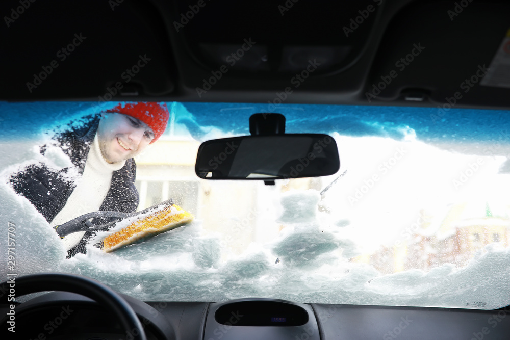 A male driver is standing in front of a car. The owner cleans the car from snow in winter. Car after snowfall.
