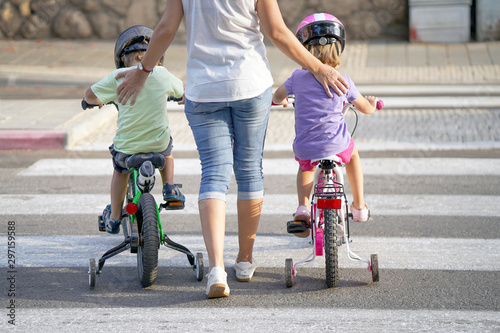 Mother goes pedestrian crossing with children on bicycles. A woman with children crossing the road in the city. Back view. 