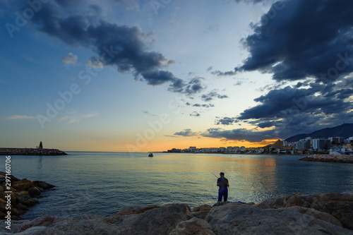 A fisherman with a fishing rod on the seashore in the evening near the port of Benalmadena, a resort on the Costa del Sol near Malaga. Andalusia, Spain.