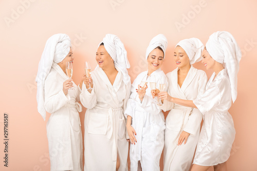 Beautiful young women in bathrobes drinking champagne on color background