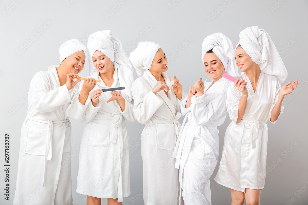 Beautiful young women in bathrobes filing nails on grey background Beautiful young women in bathrobes filing nails on grey background