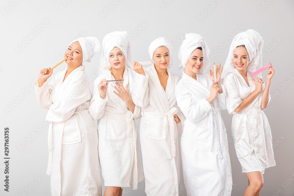 Beautiful young women in bathrobes filing nails on grey background Beautiful young women in bathrobes filing nails on grey background