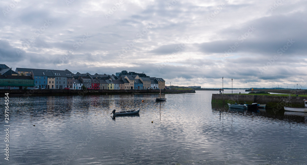 Famous view of colorful Galway city houses and River Corrib with cloudy sky and boat on water. 