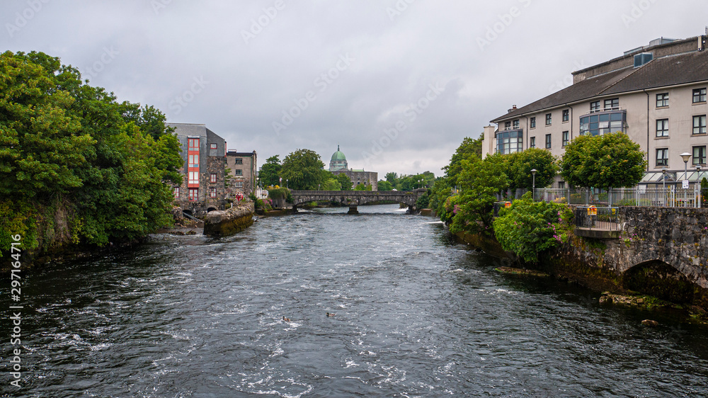 View of the River Corrib flowing through Galway City Center with the old stone buildings and walkways through the quays and view of the Cathedral