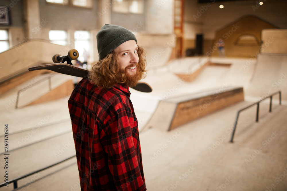 Waist up portrait of hipster man looking at camera over shoulder while posing in skating park, copy space Waist up portrait of hipster man looking at camera over shoulder while posing in skating park, copy space