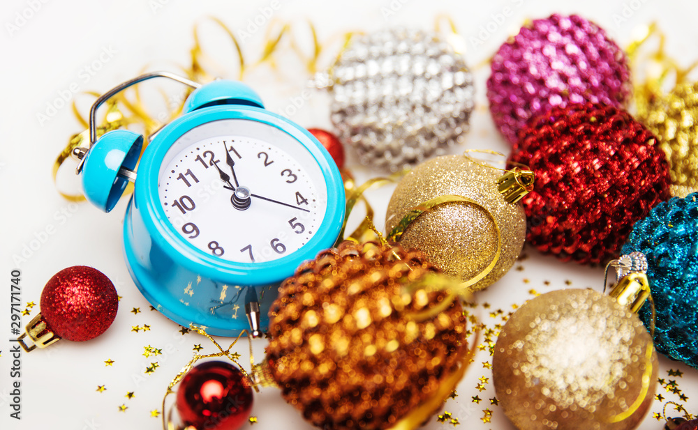 Glittery ornaments. Close up of a composition of a sky blue alarm clock,  which shows five past twelve, star-shaped golden confetti and decorations  of golden, red and silver color. Stock Photo