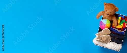 Donation box with clothing, books, children toys on blue background. Top view