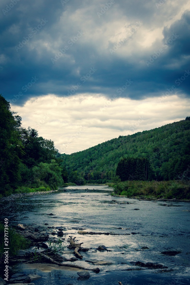 A dark moody and scenic landscape portrait of a river flowing through a forest with a mountain with dark clouds above it in the sky. A dark moody and scenic landscape portrait of a river flowing through a forest with a mountain with dark clouds above it in the sky.