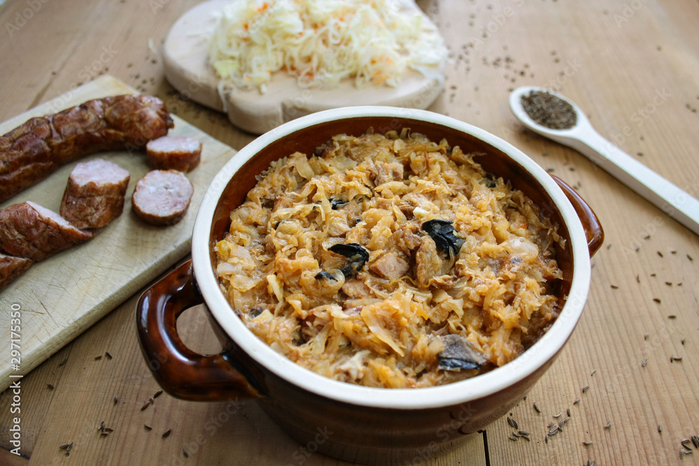 Bigos in stoneware dish and bigos ingredients: sausage, sauerkraut and cumin