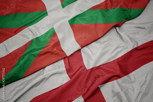 waving colorful flag of england and national flag of basque country.