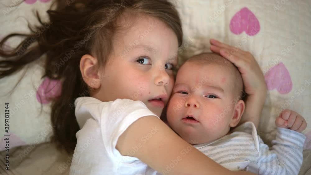 Older sister take care of the newborn baby sister. two little girls are lying on the bed. Concept of love and child care. Older sister take care of the newborn baby sister. two little girls are lying on the bed. Concept of love and child care.