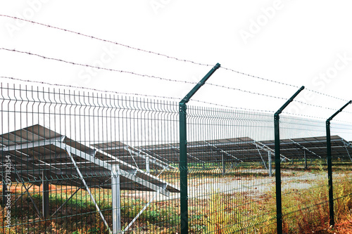 Solar panel or photovoltaic farm behind metal chainlink fence on green field with dramatic cloudy sky in North Germany