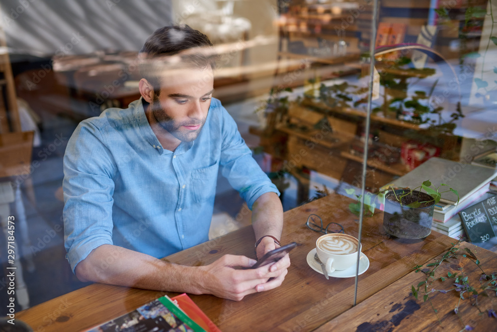 Young man using his cellphone inside of a trendy cafe