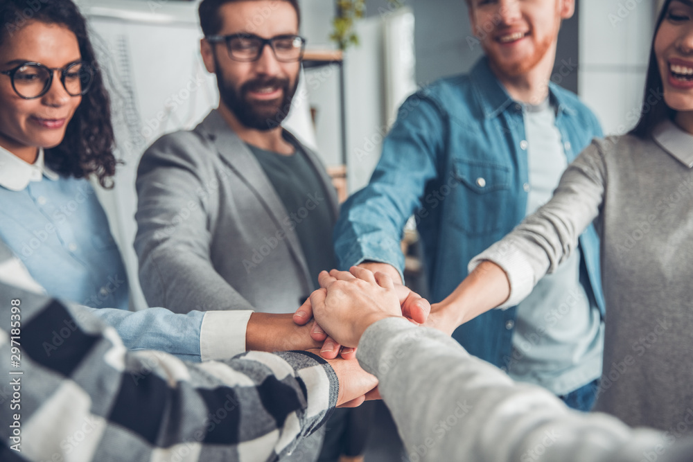 Obraz premium Startupers working at office together standing holding hands close-up smiling joyful