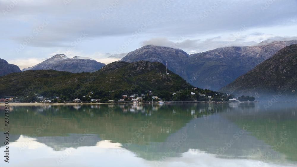 Panoramic view from the sea of Caleta Tortel in Patagonia Chile. You see some houses and boats reflected in the water, as well as the great mountains of the place