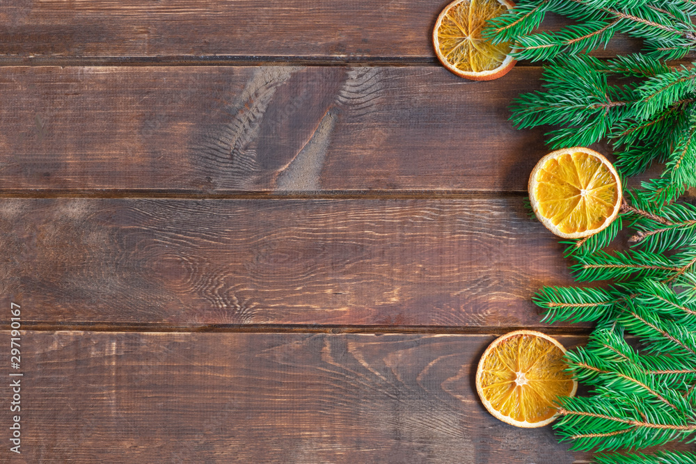 Christmas background on brown wooden table with pine branches and dry orange slices. Image with copy space, top view.
