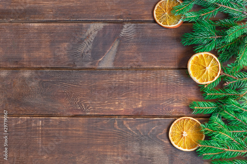 Christmas background on brown wooden table with pine branches and dry orange slices. Image with copy space, top view.