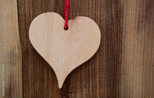 Helles Holzherz mit roter Schleife auf dunklen Holzhintergrund - Symbol f  r die Liebe