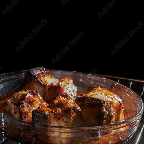 cooking ribs in the oven, on the stove. fried ribs in their own juice are fried in a baking pan languish in the oven. tasty fatty not healthy food. place text on a black background.