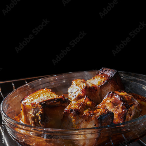 cooking ribs in the oven, on the stove. fried ribs in their own juice are fried in a baking pan languish in the oven. tasty fatty not healthy food. place text on a black background.