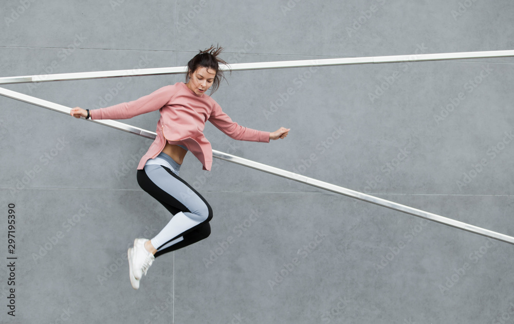 An athletic young woman is jumping, doing acrobatics, ballet, is actively involved in sports, against a concrete wall.