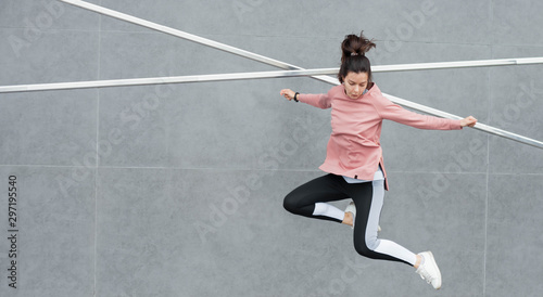 An athletic young woman is jumping, doing acrobatics, ballet, is actively involved in sports, against a concrete wall.