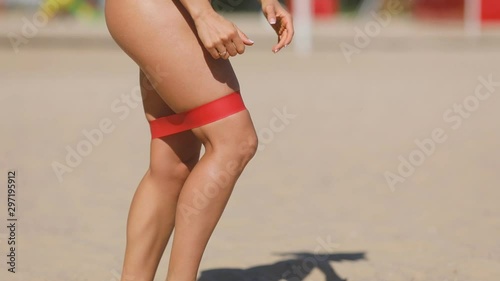Resistance band fitness woman doing lunge exercise for glutes on the beach. Athletic girl workout with fitness loop band outdoors