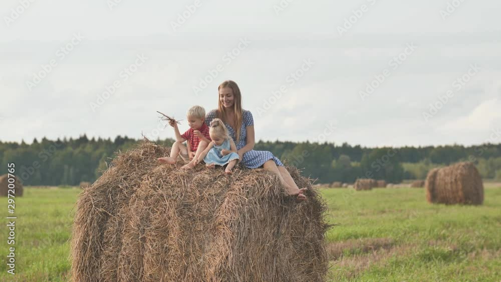 A mother with two children sits on a sheaf of straw in a field. A mother with two children sits on a sheaf of straw in a field.