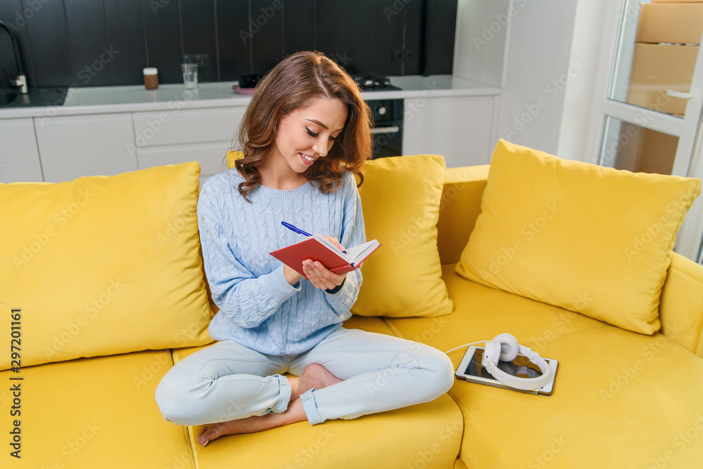 Likable young woman writing her personal notes into her diary while sitting in the modern stylish kitchen. Likable young woman writing her personal notes into her diary while sitting in the modern stylish kitchen.