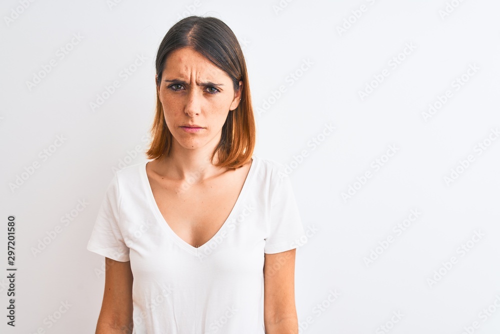 Beautiful redhead woman wearing casual white t-shirt over isolated background skeptic and nervous, frowning upset because of problem. Negative person. Beautiful redhead woman wearing casual white t-shirt over isolated background skeptic and nervous, frowning upset because of problem. Negative person.