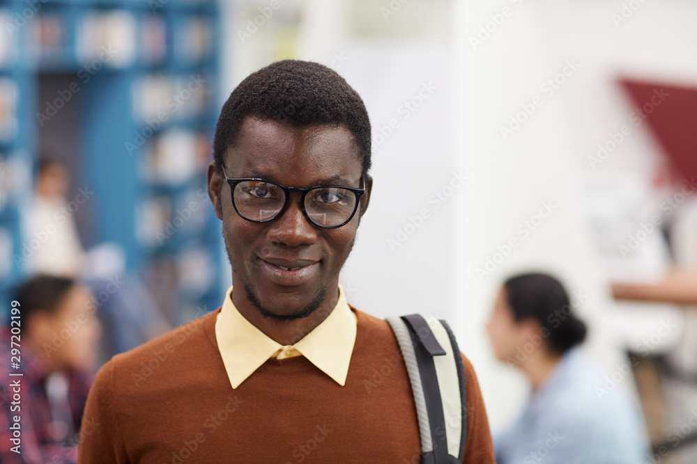 Obraz premium Head and shoulders portrait of smiling African-American student looking at camera while standing in library of modern college, copy space