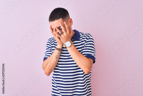 Young handsome man wearing nautical striped t-shirt over pink isolated background with sad expression covering face with hands while crying. Depression concept.