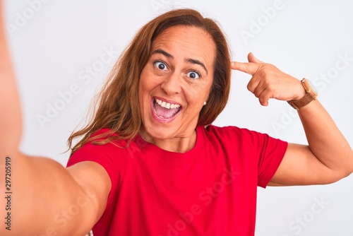 Middle age mature woman taking a selfie photo using smartphone over isolated background very happy pointing with hand and finger