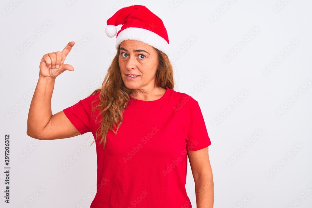 Middle age mature woman wearing christmas hat over isolated background smiling and confident gesturing with hand doing small size sign with fingers looking and the camera. Measure concept. Middle age mature woman wearing christmas hat over isolated background smiling and confident gesturing with hand doing small size sign with fingers looking and the camera. Measure concept.
