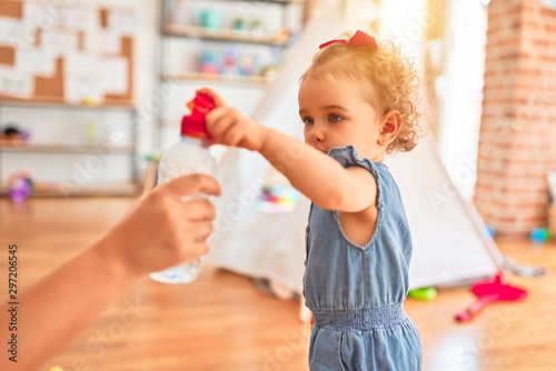 Beautiful caucasian infant playing with toys at colorful playroom. Happy and playful drinking fresh water at kindergarten.