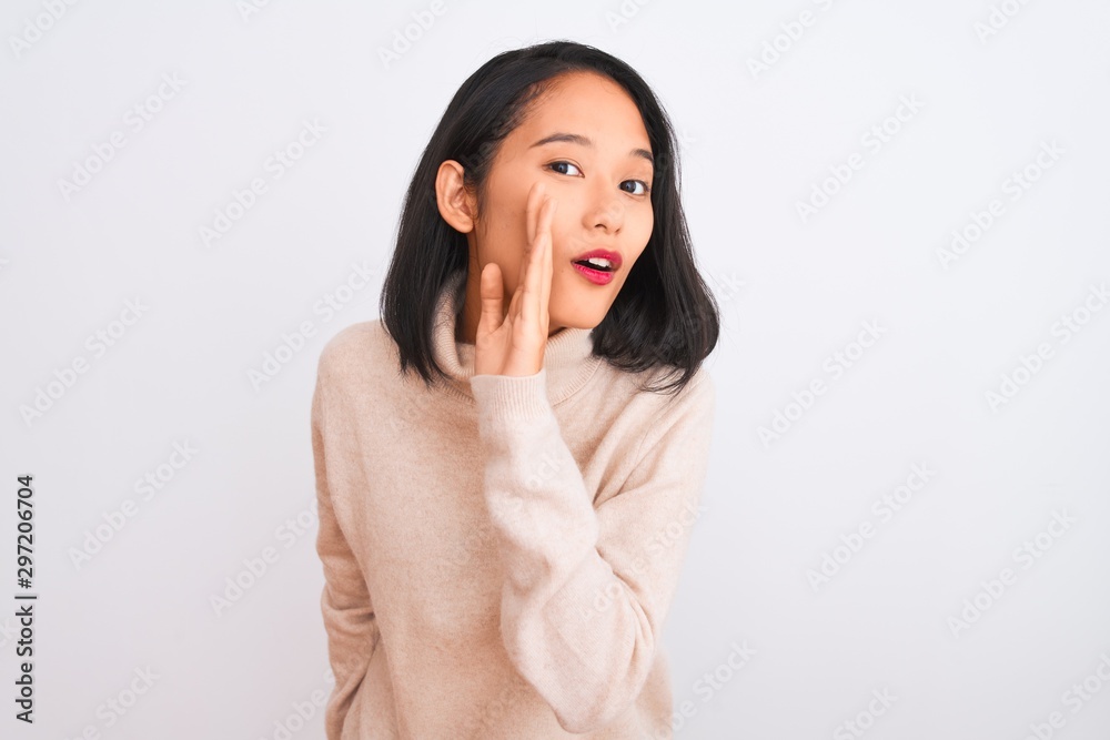Young chinese woman wearing turtleneck sweater standing over isolated white background hand on mouth telling secret rumor, whispering malicious talk conversation Young chinese woman wearing turtleneck sweater standing over isolated white background hand on mouth telling secret rumor, whispering malicious talk conversation