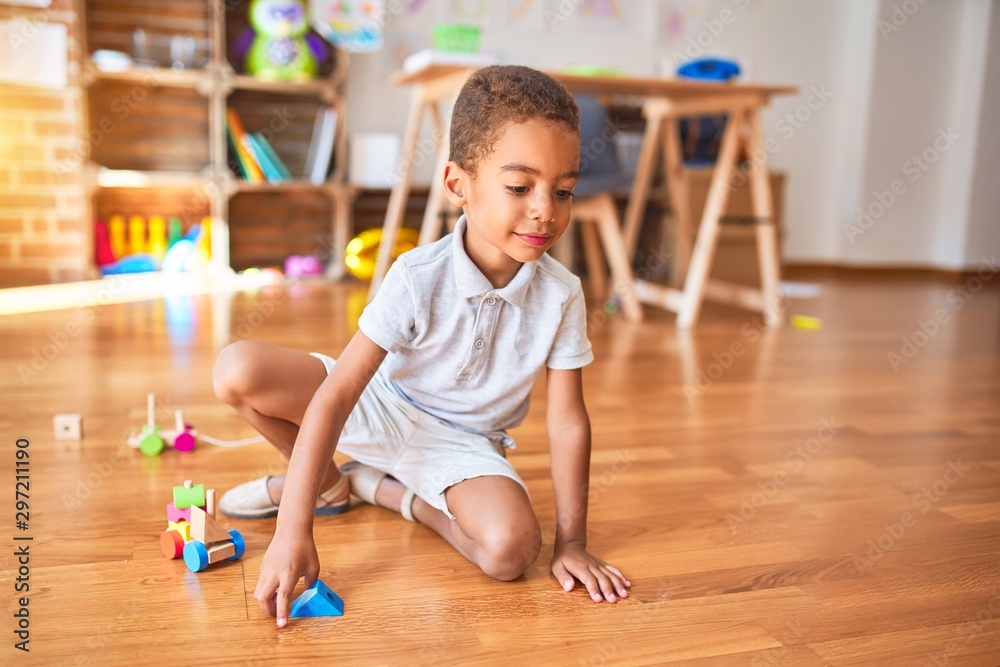 Beautiful african american toddler playing with wooden blocks train toy around lots of toys at kindergarten Beautiful african american toddler playing with wooden blocks train toy around lots of toys at kindergarten